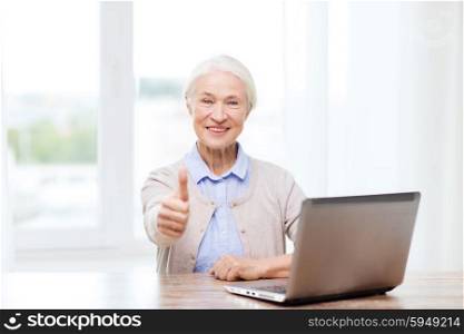 technology, age and people concept - happy senior woman with laptop computer at home showing thumbs up gesture