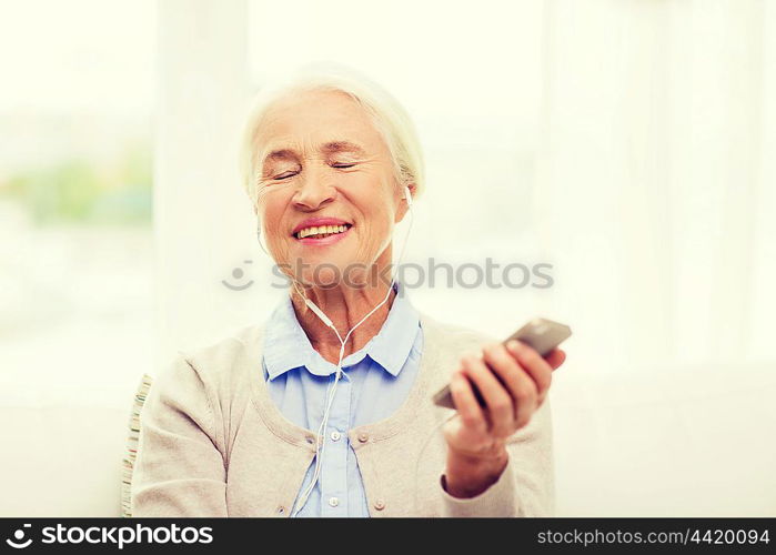 technology, age and people concept - happy senior woman with smartphone and earphones listening to music at home