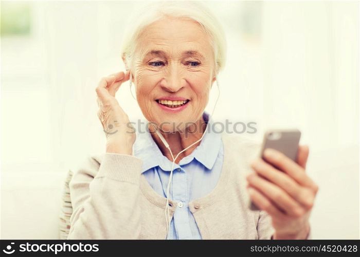 technology, age and people concept - happy senior woman with smartphone and earphones listening to music at home
