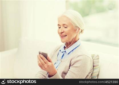 technology, age and people concept - happy senior woman with smartphone and earphones listening to music at home