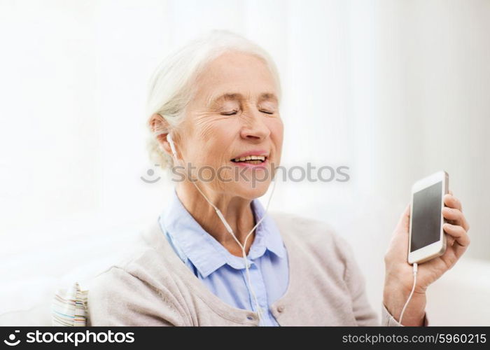 technology, age and people concept - happy senior woman with smartphone and earphones listening to music at home