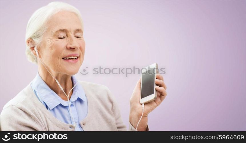 technology, age and people concept - happy senior woman with smartphone and earphones listening to music over violet background