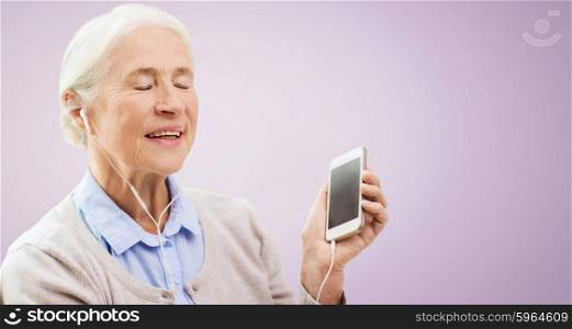 technology, age and people concept - happy senior woman with smartphone and earphones listening to music over violet background