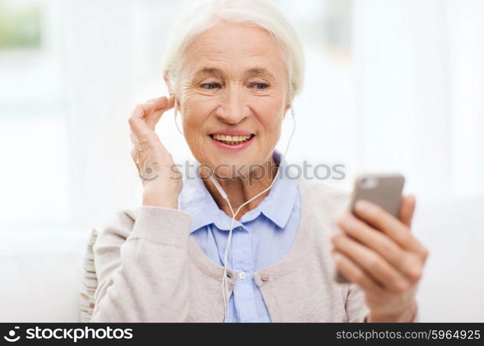 technology, age and people concept - happy senior woman with smartphone and earphones listening to music at home