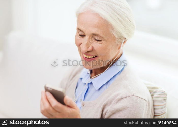 technology, age and people concept - happy senior woman with smartphone and earphones listening to music at home