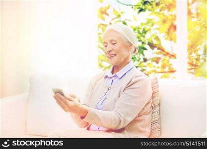 technology, age and people concept - happy senior woman with smartphone texting message at home over window with green natural background. senior woman with smartphone texting at home