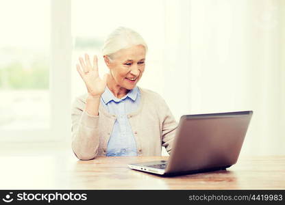 technology, age, gesture, communication and people concept - happy senior woman with laptop computer having video chat at home and waving hand