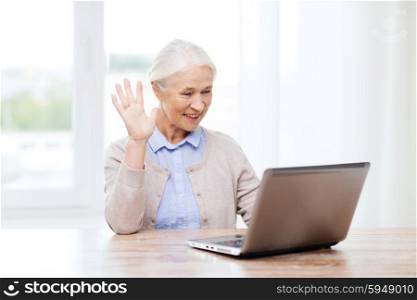 technology, age, gesture, communication and people concept - happy senior woman with laptop computer having video chat at home and waving hand