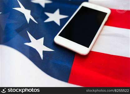 technology, american independence day, patriotism and nationalism concept - close up of smartphone computer on american flag