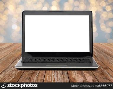 technology and advertisement concept - laptop computer with blank white screen on wooden table over christmas lights background. laptop computer with white screen over lights