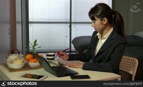 Technology and Asian people working at home with pc, beautiful Japanese young business woman at work with laptop computer and newspaper, having breakfast in living room, busy girl typing on keyboard