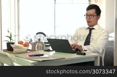 Technology and Asian people working at home with pc, young business man at work with laptop computer while having breakfast in living room, businessman talking on mobile phone, busy male manager
