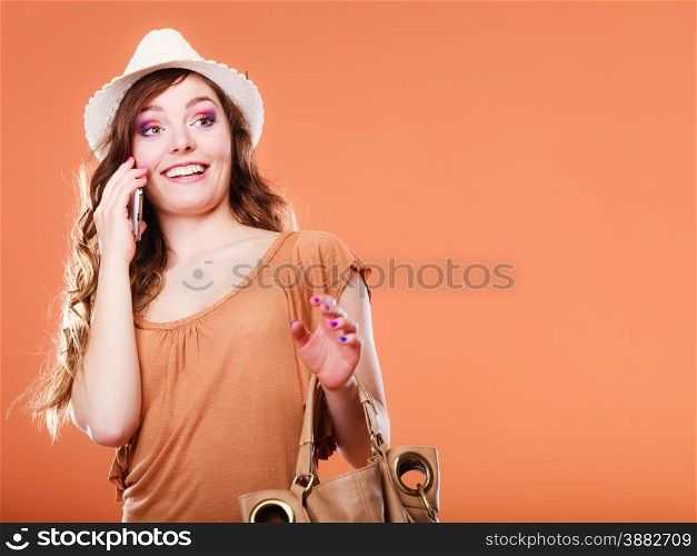 Technology and communication. Attractive summer woman talking on mobile phone holding handbag orange background