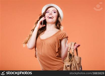 Technology and communication. Attractive summer woman talking on mobile phone holding handbag orange background