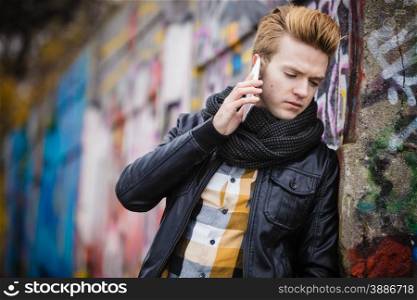 Technology and communication. Closeup young fashion man talking on mobile cell phone using smartphone outdoor graffiti wall background