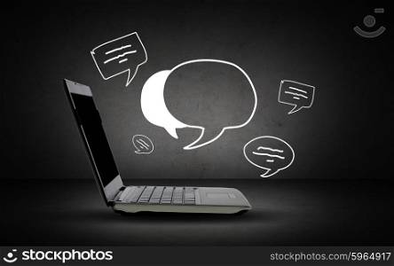 technology and communication concept - open laptop computer with blank screen and text bubbles over dark gray background. laptop computer with blank screen and text bubbles