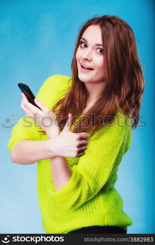 Technology and communication. Woman teenage girl texting on mobile phone, using smartphone reading sms, thumb up hand gesture on blue