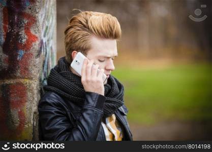 Technology and communication. Young fashion man talking on mobile cell phone using smartphone outdoor