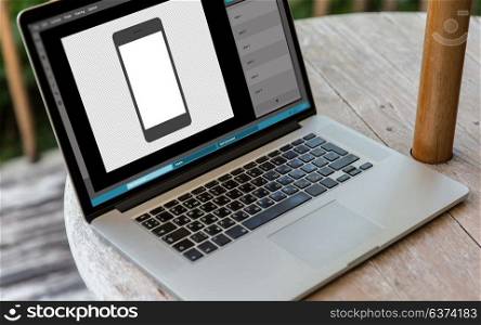 technology and design concept - laptop computer with smartphone image in graphics editor on table. laptop with smartphone image in graphics editor
