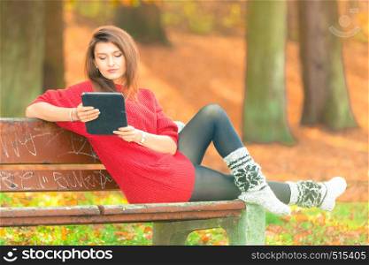 Technology and education. Woman relaxing in autumnal park sitting on bench with tablet. Pretty fashionable female student learn on fresh air.. Woman on bench in park with tablet.