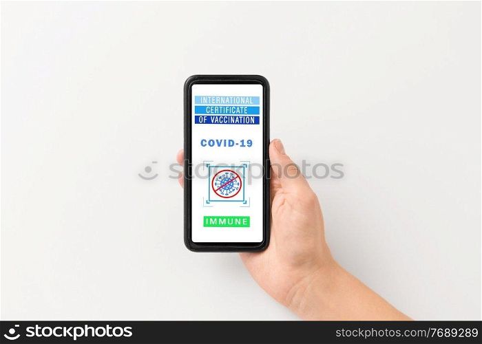 technology and health care concept - close up of hand holding and showing smartphone with international certificate of vaccination on screen over grey background. hand holding phone with certificate of vaccination