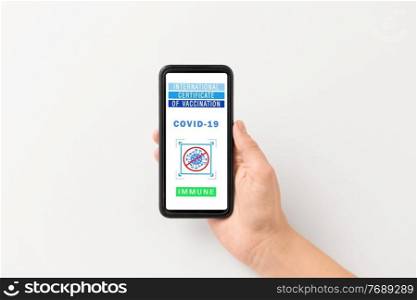 technology and health care concept - close up of hand holding and showing smartphone with international certificate of vaccination on screen over grey background. hand holding phone with certificate of vaccination