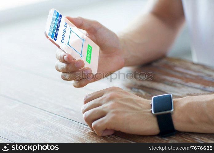 technology and health care concept - close up of male hands with international certificate of vaccination on transparent smartphone’s screen and smart watch on table. hand with certificate of vaccination on smartphone
