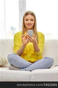 technology and internet concept - smiling young woman or teenage girl with smartphone sitting on couch at home. young woman or teen girl with smartphone at home