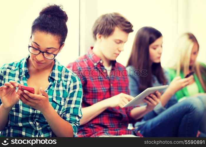 technology and internet concept - students looking into phones and tablet pc at school