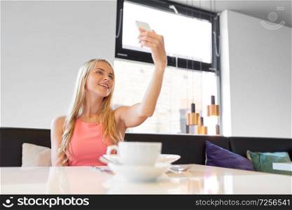 technology and leisure concept - happy woman with smartphone taking selfie at restaurant. woman with smartphone taking selfie at restaurant