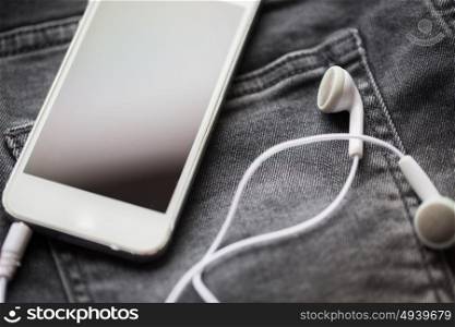 technology and music concept - smartphone and earphones on pocket of denim pants or jeans. smartphone and earphones on denim or jeans pocket