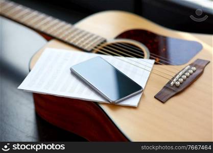 technology and music writing concept - close up of acoustic guitar, music book and smartphone. close up of guitar, music book and smartphone