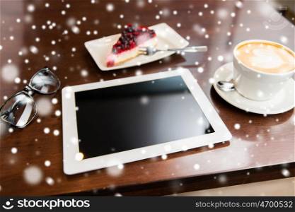 technology and object concept - close up of tablet pc computer, eyeglasses, coffee cup and berry cake on table over snow