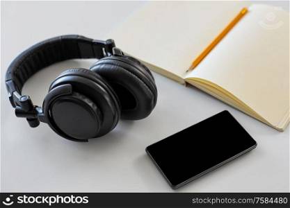 technology and objects concept - headphones, smartphone and notebook with pencil on white background. headphones, smartphone and notebook with pencil