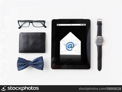 technology and objects concept - tablet pc computer with e-male message icon, wallet, eyeglasses, bowtie and wristwatch on table