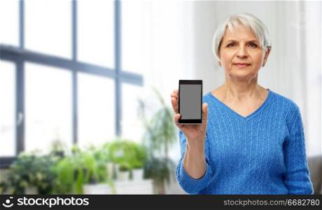 technology and old people concept - senior woman showing smartphone over home living room background. senior woman showing smartphone at home