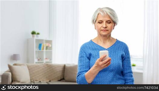 technology and old people concept - senior woman using smartphone over home living room background. senior woman using smartphone at home