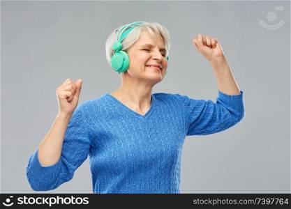 technology and old people concept - smiling senior woman in glasses and headphones listening to music over grey background. senior woman in headphones listening to music