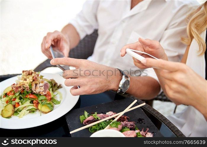 technology and people and concept - close up of couple with smatphones taking picture of food at restaurant terrace. couple with smatphones photographing food
