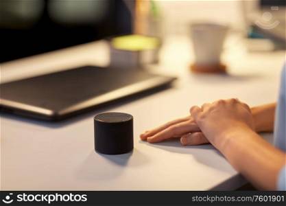 technology and people concept - close up of hand with smart speaker on table at night office. close up of hand with smart speaker at office