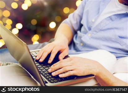 technology and people concept - close up of man typing on laptop keyboard over christmas lights background. close up of man typing on laptop keyboard