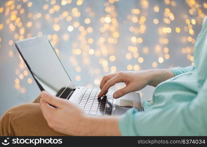 technology and people concept - close up of man typing on laptop keyboard over holidays lights background. close up of man typing on laptop keyboard