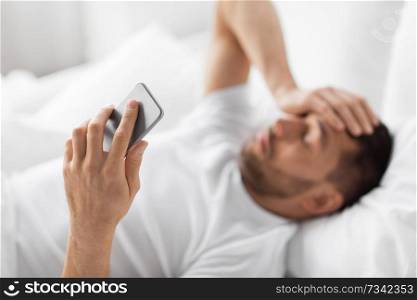technology and people concept - hand of young man with smartphone in bed at home in morning. hand of young man with smartphone in bed