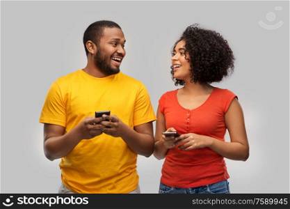 technology and people concept - happy african american couple with smartphones over grey background. happy african american couple with smartphones