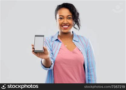 technology and people concept - happy african american woman showing blank screen of smartphone over grey background. happy african american woman showing smartphone