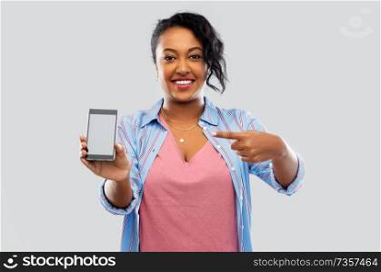 technology and people concept - happy african american woman showing blank screen of smartphone over grey background. happy african american woman showing smartphone