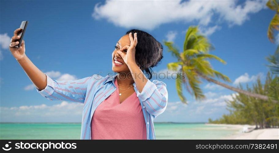 technology and people concept - happy african american woman taking selfie by smartphone over tropical beach background in french polynesia. african american woman taking selfie by smartphone