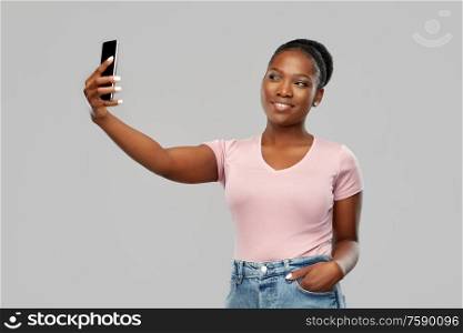 technology and people concept - happy african american woman taking selfie by smartphone over grey background. african american woman taking selfie by smartphone