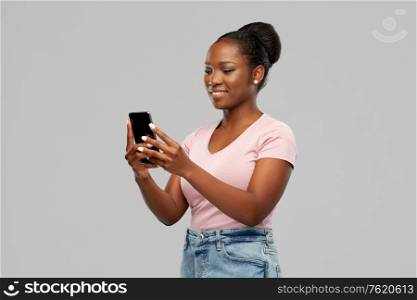 technology and people concept - happy african american woman using smartphone over grey background. happy african american woman using smartphone