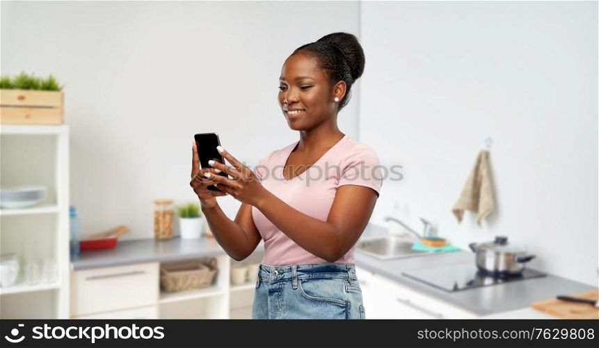 technology and people concept - happy african american woman using smartphone over home kitchen background. happy african american woman using smartphone